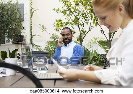 Businessman and colleague seated at table in hotel courtyard View Large Photo Image Picture - Businessman and colleague seated at table in hotel courtyard. Fotosearch
