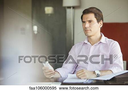 Businessman holding smartphone in office, looking away in thought View Large Photo Image Stock Photography - Businessman holding smartphone in office, looking away in thought. Fotosearch
