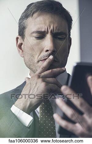 Businessman looking at digital tablet with furrowed brow View Large Photo Image Stock Photograph - Businessman looking at digital tablet with furrowed brow. Fotosearch
