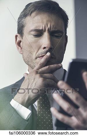 Businessman looking at digital tablet with furrowed brow View Large Photo Image Stock Photograph - Businessman looking at digital tablet with furrowed brow. Fotosearch
