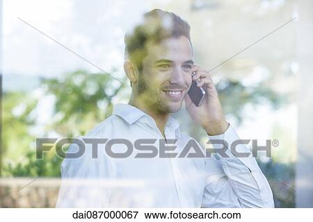 Businessman looking out of window from office while using cell phone View Large Photo Image Stock Photo - Businessman looking out of window from office while using cell phone. Fotosearch