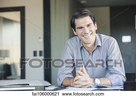 Businessman sitting at desk, smiling, portrait View Large Photo Image Stock Image - Businessman sitting at desk, smiling, portrait. Fotosearch