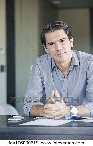 Businessman sitting at desk with clasped hands, portrait View Large Photo Image Stock Photo - Businessman sitting at desk with clasped hands, portrait. Fotosearch
