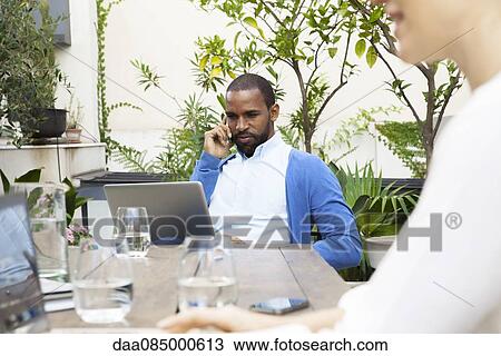 Stock Image - Businessman using laptop whiile making phone call outdoors. Fotosearch