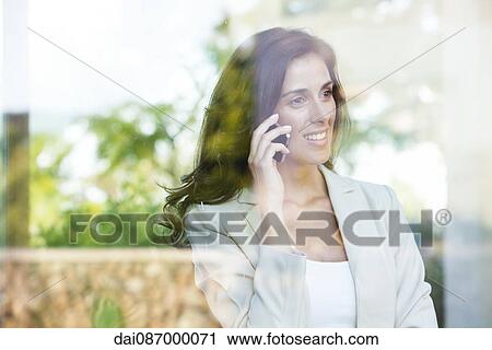 Businesswoman looking out of window from office while using cell phone View Large Photo Image Stock Image - Businesswoman looking out of window from office while using cell phone. Fotosearch