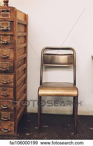 Stock Photo - Chair next to old chest of drawers. Fotosearch