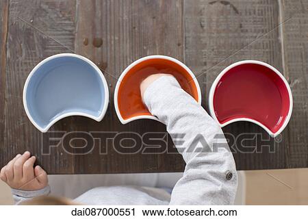 Stock Image - Child reaching into bowl, overhead view. Fotosearch