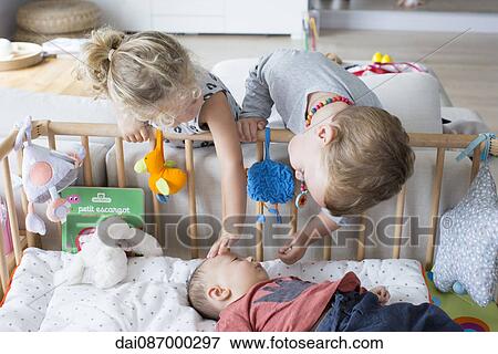 Children leaning over the side of baby brother's crib View Large Photo Image Stock Photo - Children leaning over the side of baby brother's crib. Fotosearch