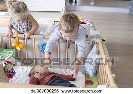 Stock Photograph - Children leaning over the side of baby brother's crib. Fotosearch