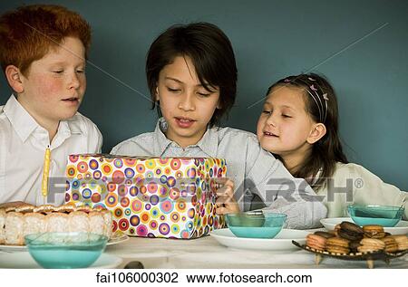 Stock Image - Children looking at wrapped gift at birthday party. Fotosearch