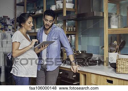 Stock Photo - Couple in kitchen looking at digital tablet together. Fotosearch