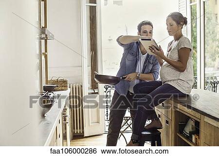 Couple referencing digital tablet while preparing meal View Large Photo Image Stock Photograph - Couple referencing digital tablet while preparing meal. Fotosearch