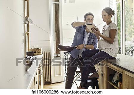 Couple referencing digital tablet while preparing meal View Large Photo Image Stock Photograph - Couple referencing digital tablet while preparing meal. Fotosearch