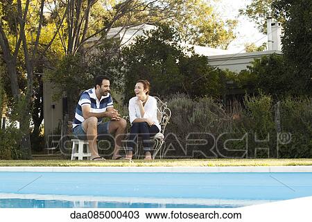 Couple relaxing together by backyard swimming pool View Large Photo Image Stock Image - Couple relaxing together by backyard swimming pool. Fotosearch