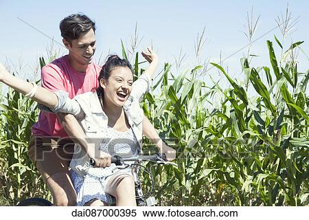 Stock Photography - Couple riding bike together, woman with arms outstretched. Fotosearch