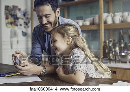 Father and daughter looking at smartphone together View Large Photo Image Picture - Father and daughter looking at smartphone together. Fotosearch