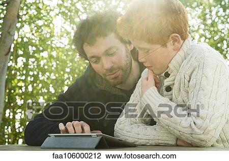 Father and son looking at digital tablet together View Large Photo Image Stock Image - Father and son looking at digital tablet together. Fotosearch
