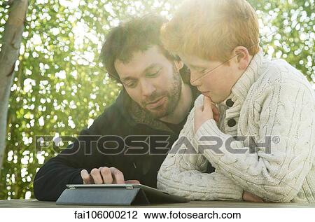 Father and son looking at digital tablet together View Large Photo Image Stock Image - Father and son looking at digital tablet together. Fotosearch