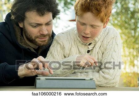 Stock Photograph - Father and son looking at digital tablet together. Fotosearch