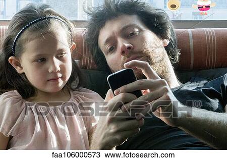 Father and young daughter looking at smartphone together View Large Photo Image Stock Image - Father and young daughter looking at smartphone together. Fotosearch