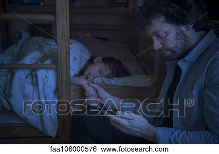 Stock Photograph - Father checking smartphone while comforting sick daughter. Fotosearch