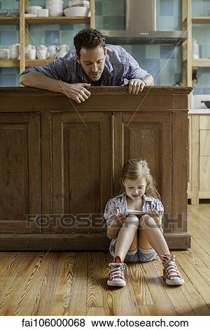 Stock Photo - Father looking on as daughter plays video game. Fotosearch