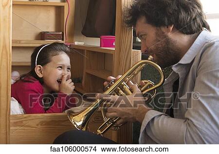 Picture - Father playing trumpet for little girl lying in bed. Fotosearch
