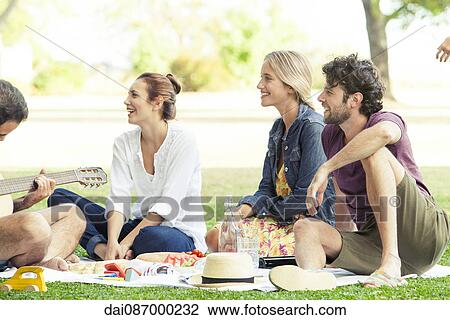 Firends listening to man playing guitar while picnicking in park View Large Photo Image Stock Image - Firends listening to man playing guitar while picnicking in park. Fotosearch
