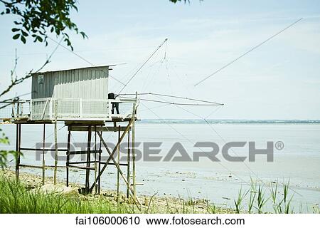 Stock Image - Fishing hut on stilts near water's edge. Fotosearch