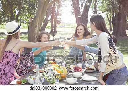 Friends clinking glasses during outdoor meal at park View Large Photo Image Stock Image - Friends clinking glasses during outdoor meal at park. Fotosearch