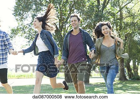 Friends holding hands running carefree through a park View Large Photo Image Stock Photo - Friends holding hands running carefree through a park. Fotosearch