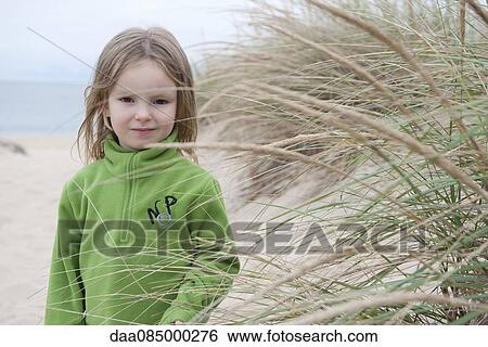 Stock Photograph - Girl behind dune grass at beach, portrait. Fotosearch