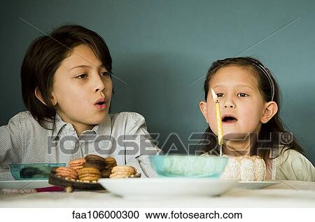 Stock Image - Girl blowing out candle on birthday cake. Fotosearch