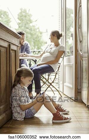 Girl engrossed in video game while parents chat in background View Large Photo Image Stock Image - Girl engrossed in video game while parents chat in background. Fotosearch