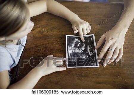 Girl looking at ultrasound photo of her new sibling to be View Large Photo Image Stock Photography - Girl looking at ultrasound photo of her new sibling to be. Fotosearch