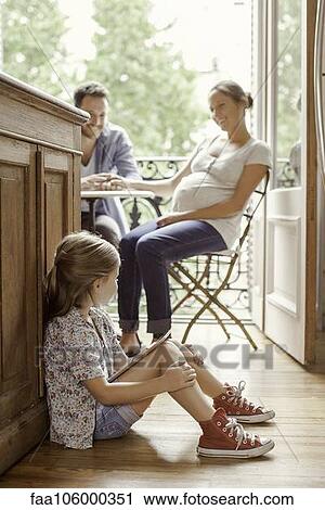 Girl sitting on floor with digital tablet as parents chat in background View Large Photo Image Stock Image - Girl sitting on floor with digital tablet as parents chat in background. Fotosearch