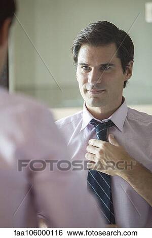 Stock Photograph - Man adjusting his tie in mirror. Fotosearch