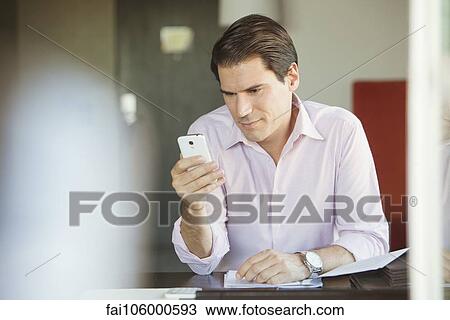 Stock Image - Man checking smartphone in office. Fotosearch