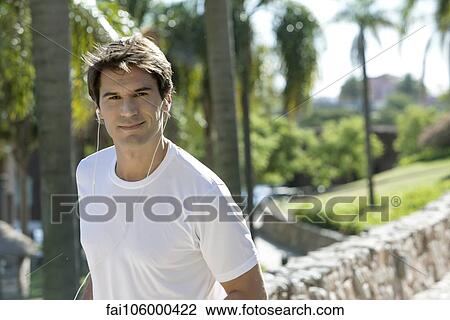 Man listening to earphones in park, portrait View Large Photo Image Stock Image - Man listening to earphones in park, portrait. Fotosearch