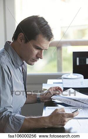 Man looking at smartphone while reading document View Large Photo Image Stock Photograph - Man looking at smartphone while reading document. Fotosearch