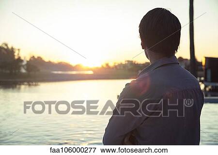 Stock Photo - Man looking at sunset, rear view. Fotosearch