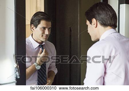 Man looking in mirror, adjusting necktie View Large Photo Image Stock Image - Man looking in mirror, adjusting necktie. Fotosearch