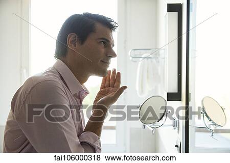 Stock Photo - Man looking in mirror, applying moisurizer to face. Fotosearch