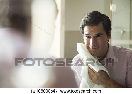 Stock Photo - Man looking in mirror, drying his face with a towel. Fotosearch