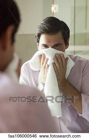 Stock Photograph - Man looking in mirror, drying his face with a towel. Fotosearch