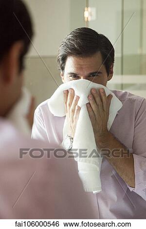 Stock Photograph - Man looking in mirror, drying his face with a towel. Fotosearch