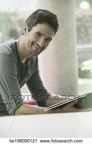 Stock Image - Man looking through magazine while waiting in waiting room. Fotosearch
