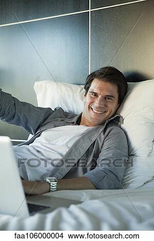 Picture - Man lying on bed, smiling cheerfully, portrait. Fotosearch
