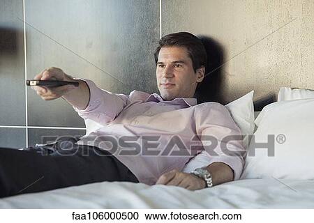 Man lying on bed, watching TV View Large Photo Image Stock Image - Man lying on bed, watching TV. Fotosearch