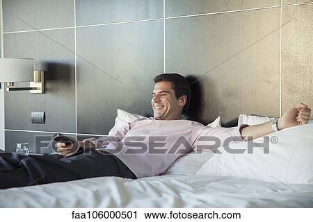 Stock Image - Man lying on bed, watching TV. Fotosearch